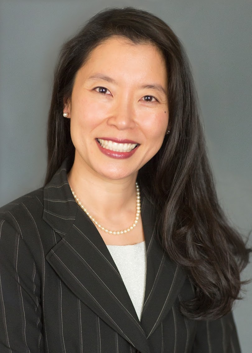 Professional portrait of a smiling woman in business attire with a pearl necklace.