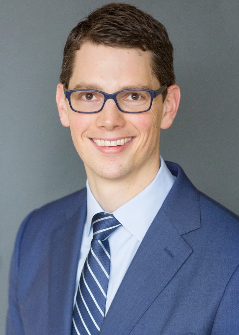 Professional man with a friendly smile wearing a blue suit and striped tie.