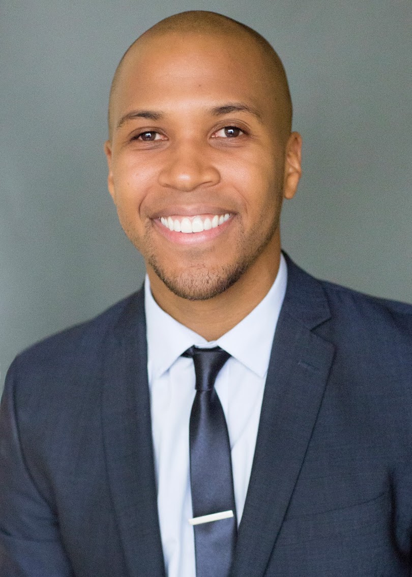 A professional portrait of a smiling man in a suit and tie.