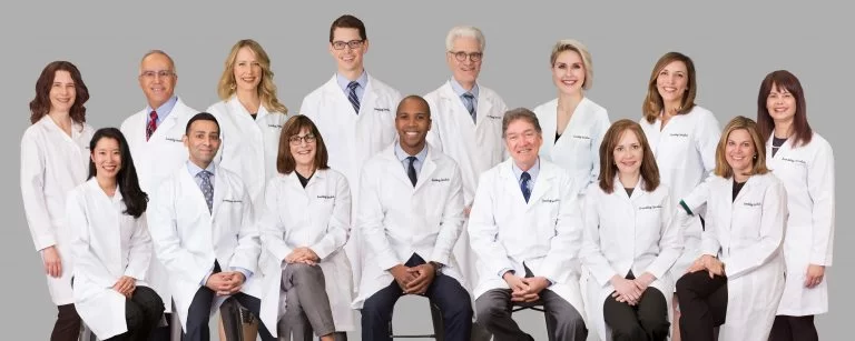 A team of medical professionals in white coats, smiling and posing together for a group portrait.