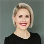 A professional headshot of a smiling woman with short blonde hair and striking red lipstick.