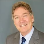 A portrait of a smiling older gentleman with graying hair, wearing a business suit and tie.