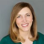 A professional headshot of a smiling woman with shoulder-length hair wearing a green top.