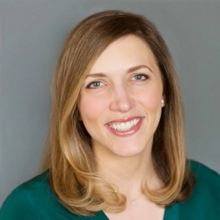 A professional headshot of a smiling woman with shoulder-length hair wearing a green top.