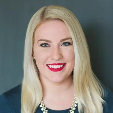 Professional woman with a confident smile, wearing a necklace and a blue jacket.