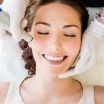 A smiling woman receiving a facial treatment with a specialized device, exuding relaxation and contentment.