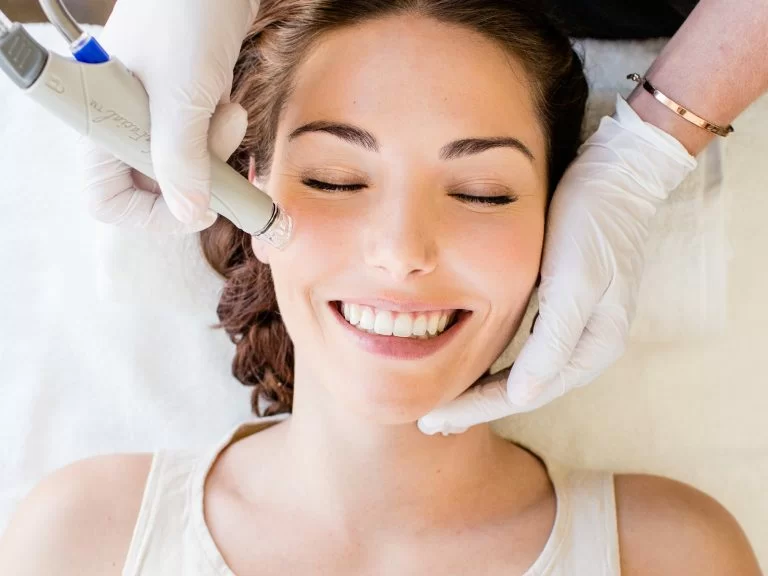 A smiling woman receiving a facial treatment with a specialized device, exuding relaxation and contentment.