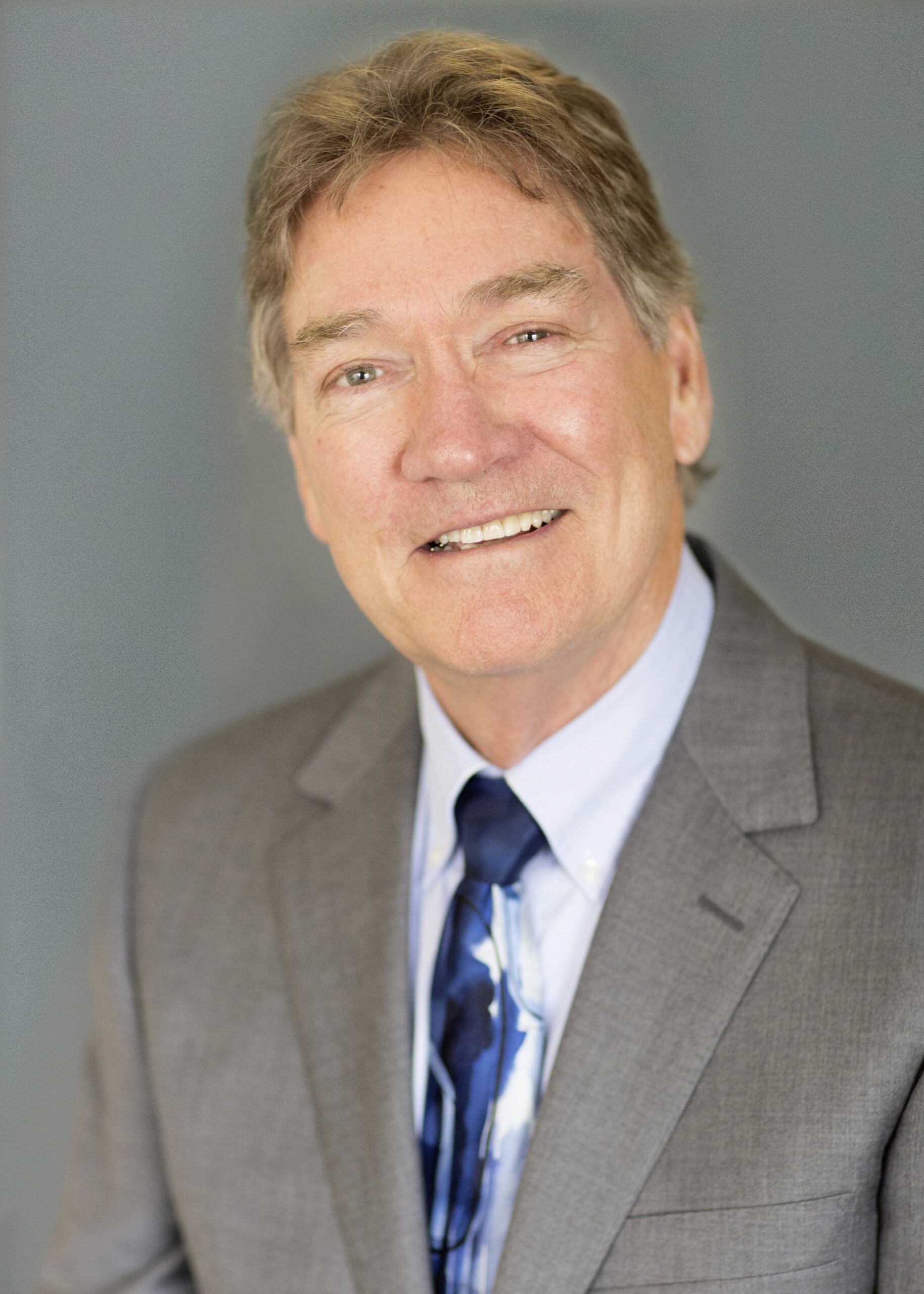 Professional portrait of a smiling businessman in a gray suit with a blue tie.